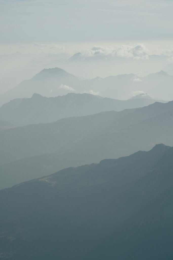 Ethereal view of alpine mountains enveloped in mist with a tranquil, hazy atmosphere.